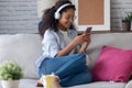 Beautiful young woman listening to music with headphones while using her smartphone sitting on sofa at home Royalty Free Stock Photo