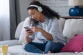 Beautiful young woman listening to music with headphones while using her smartphone sitting on sofa at home Royalty Free Stock Photo