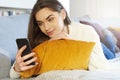 Smiling young woman text messaging while relaxon on sofa at home