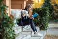 Beautiful young woman reading a book while sitting with her lovely golden retriever dog in the park in autumn Royalty Free Stock Photo