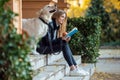 Beautiful young woman reading a book while sitting with her lovely golden retriever dog in the park in autumn Royalty Free Stock Photo