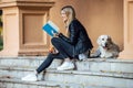 Beautiful young woman reading a book while sitting with her lovely golden retriever dog in the park in autumn Royalty Free Stock Photo