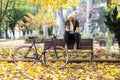 Beautiful young woman sending messages with her smart phone while drinking coffee sitting on a bench in the park in autumn Royalty Free Stock Photo