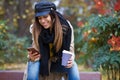 Beautiful young woman using her mobile phone while drinking coffee and sitting in a bench in the street Royalty Free Stock Photo