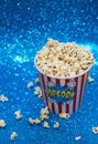 Shot  of a big paper cup filled with popcorn on a shiny blue surface Royalty Free Stock Photo