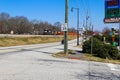 A shot of a black and orange train on the tracks near a street with cars driving with yellow and green grass