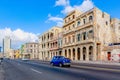Shot of a blue car passing a street in La Havana with historic buildings in the background
