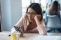 Boring young business woman sending messages with mobile phone while sitting in modern startup office