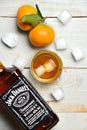 A shot and a bottle of whiskey on wooden table surrounded by ice cubes and tangerines Royalty Free Stock Photo