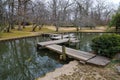 A shot of a brown wooden foot bridge over a still green lake in a Japanese garden surrounded by yellow winter grass Royalty Free Stock Photo