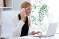 Business young woman talking on the mobile phone while using her laptop in the office. Royalty Free Stock Photo