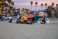 A shot of a colored homeless encampment on the beach with silky brown sand, people relaxing and powerful clouds at sunset