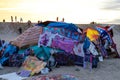 A shot of a colorful homeless encampment on the beach with silky brown sand, people relaxing and powerful clouds at sunset