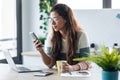 Concentrated young business woman using her mobile phone while working with computer in the kitchen at home Royalty Free Stock Photo