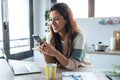 Concentrated young business woman using her mobile phone while working with computer in the kitchen at home Royalty Free Stock Photo