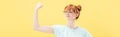 Shot of confident pleased redhead girl in glasses and t-shirt holding fist up isolated on yellow