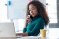 Confident young business woman talking on mobile phone while working with her laptop in the office Royalty Free Stock Photo