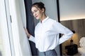 Confident young businesswoman looking sideways standing near the window at hotel room