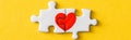 Shot of connected jigsaw puzzle pieces with drawn red heart isolated on yellow