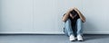 Shot of depressed man sitting on floor near white wall and holding hands on head