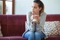 Depressed young woman thinking about her problems while drinking coffee on sofa at home Royalty Free Stock Photo