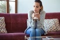 Depressed young woman thinking about her problems while drinking coffee on sofa at home Royalty Free Stock Photo