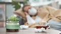 On the road to recovery. Shot of dirty tissues and a cup of tea on a table next to a woman lying sick at home.