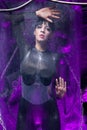 Shot of a futuristic young person posing near glass space capsule with wires and purple neon light on black background