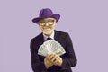 Handsome mature man dressed in suit holding money fan isolated on purple color background Royalty Free Stock Photo