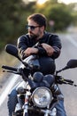 Handsome bearded biker looking to sideways while sitting on his motorbike and holding helmet