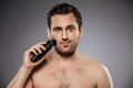 Shot of handsome man shaving his face with electric shaver, making morning procedure in bathroom against gray wall Royalty Free Stock Photo