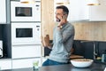 Handsome mature business man eating take away noodles while using smartphone in the kitchen at home Royalty Free Stock Photo