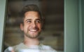 Make everyday an awesome one. Shot of a handsome young man looking out of a window at home and smiling. Royalty Free Stock Photo