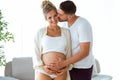 Handsome young man touching belly of beautiful pregnant woman while man kissing to his wife at home Royalty Free Stock Photo