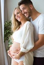 Handsome young man touching belly of beautiful pregnant woman while standing at home.