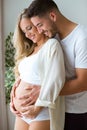 Handsome young man touching and looking belly of beautiful pregnant woman while standing at home