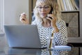 Shot happy businesswoman sitting at desk behind her laptop and talking with somebody on her mobile phone while working from home. Royalty Free Stock Photo