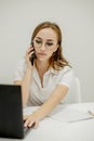 Shot happy businesswoman sitting at desk behind her laptop and talking with somebody on her mobile phone while working Royalty Free Stock Photo