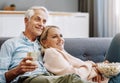 Turning home into their very own cinema. Shot of a happy mature couple relaxing together with wine and popcorn on the Royalty Free Stock Photo