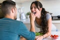 Happy young couple enjoying lunch while handsome man is feeding with yogurt his wife in the kitchen at home. Royalty Free Stock Photo