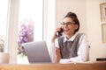 Attractive happy woman talking with somebody on her mobile phone while sitting behind laptop and working Royalty Free Stock Photo