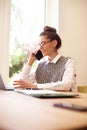 Attractive happy woman talking with somebody on her mobile phone while sitting behind laptop and working Royalty Free Stock Photo