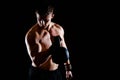 Shot of healthy muscular young man doing weight exercise with dumbbells against dark background. Royalty Free Stock Photo