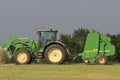 John Deere Tractor and Baler in a farm field with a stormy sky in the background.