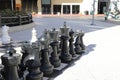 A shot of a large black and white chess set on the sidewalk surrounded by lush green plants, bare winter trees and shops Royalty Free Stock Photo