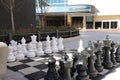 A shot of a large black and white chess set on the sidewalk surrounded by lush green plants, bare winter trees and shops Royalty Free Stock Photo