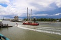 A shot of a large red and white fishing boat sailing on the Savannah River with vast green river water and blue sky with cloud