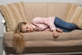 A little blonde girl with long hair wearing pink shirt and jeans  lies on the couch and is sad Royalty Free Stock Photo