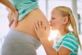 Were going to have so much fun, little baby. Shot of a little girl kissing her mothers pregnant belly at home. Royalty Free Stock Photo