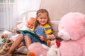 Shot of a little girl reading a book with her toys around her